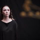 A woman in a black dress with bloody tears coming from her eyes stands in front of a black background in a scene from horror film Agnes.
